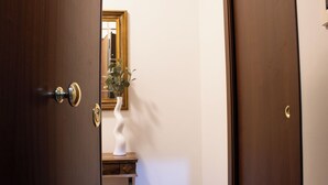 Una puerta de madera con manija de latón y cerradura, que da a un cuarto con un espejo, un florero blanco y una pequeña mesa de madera.