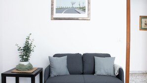 Un salón con un sofá gris, una mesita con una planta y un cuadro en la pared.