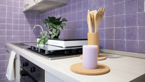 Una cocina con estufa a gas, encimera blanca, planta en maceta, utensilios de madera y posavasos de corcho.