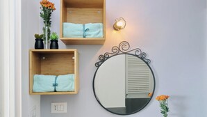 A bathroom with wooden shelves holding towels, a round mirror with a decorative frame, and a wall-mounted light fixture.