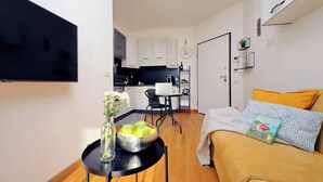 A compact living space with a kitchen, dining area, and a sofa with a book and decorative pillows.