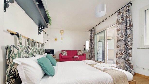Une chambre à coucher avec un lit, un canapé rouge, une télévision et une fenêtre avec des rideaux.