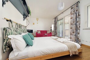 Ein Schlafzimmer mit einem Bett, einem roten Sofa, einem Fernseher und einem Fenster mit Vorhängen.