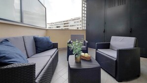 Un balcon agrémenté de meubles en osier, d’un vase avec des plantes et d’un panier contenant des bougies.