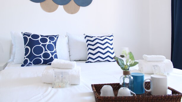 A neatly made bed with white linens, two pillows with blue patterns, a blue mug, a white mug, and a basket with toiletries. - La Casa di Annamaria by Domus&Dimore (Pulsano)
