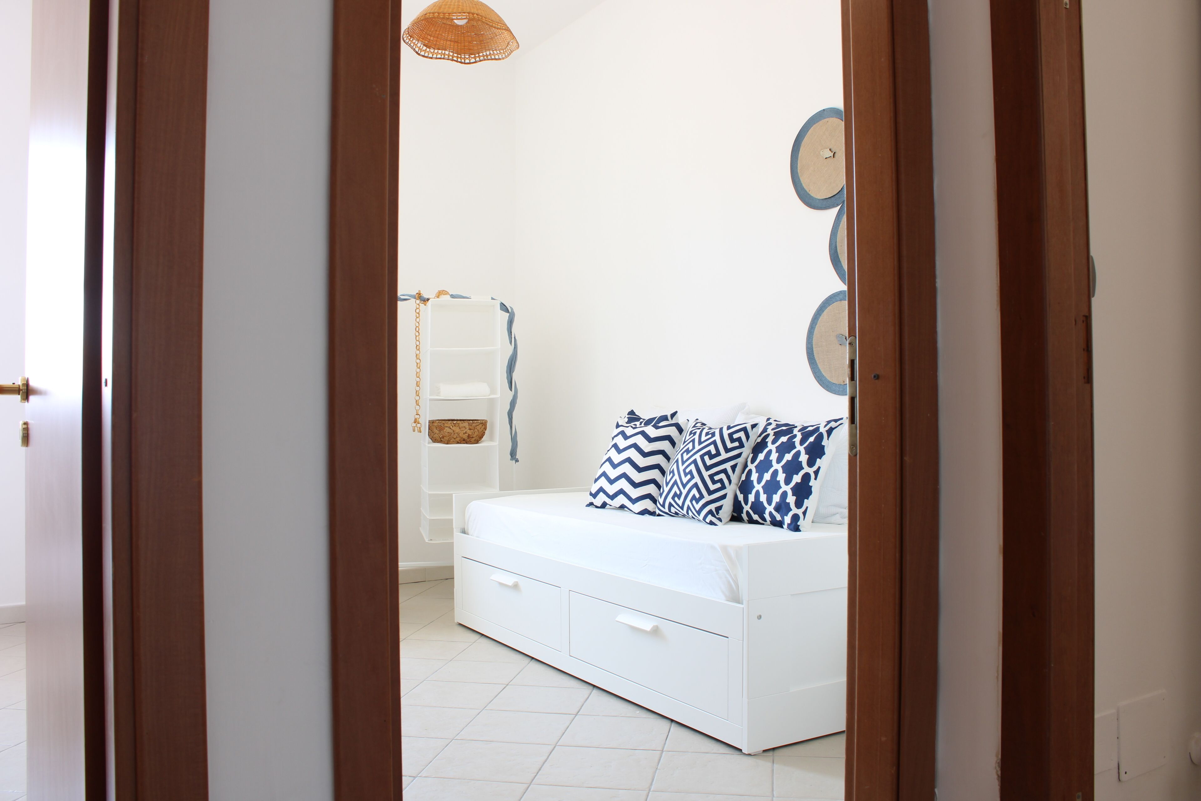 A white bed with patterned pillows, a wooden door frame, and a white wall with circular decorations.