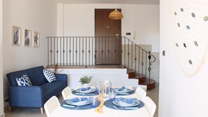 A dining area with a white table set for four, blue tableware, and a blue sofa with patterned cushions. A staircase with a railing is visible in the background. - La Casa di Annamaria by Domus&Dimore (Pulsano)