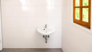 A bathroom with a white sink, grey tiles, and a window with a wooden frame. - Charming Studio in a Villa Stay for 4 with Lush Garden Access (Wien)