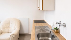 A modern kitchen with a stainless steel sink, wooden countertop, and a white chair. - Charming Studio in a Villa Stay for 4 with Lush Garden Access (Wien)