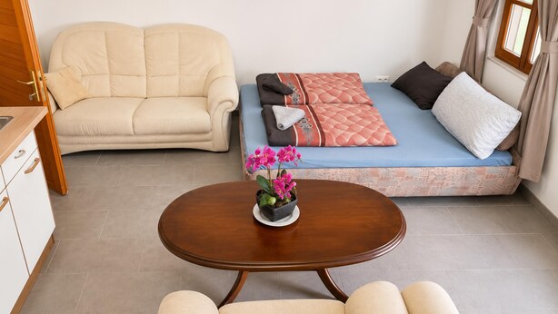 A compact living space with a sofa, a bed with patterned bedding, a small table with a flower, and a window with curtains. - Charming Studio in a Villa Stay for 4 with Lush Garden Access (Wien)