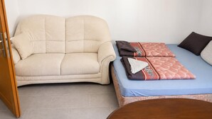 A room with a beige sofa, a bed with patterned bedding, and a wooden door. - Charming Studio in a Villa Stay for 4 with Lush Garden Access (Wien)
