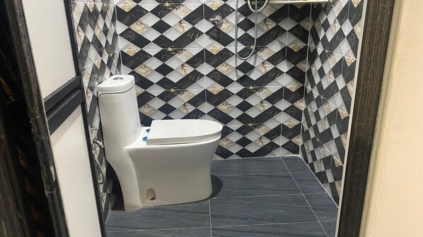 Un baño con inodoro, baldosas blancas y negras en estampado y suelo oscuro.