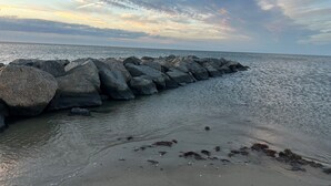 A rocky breakwater extending into calm waters with a clear sky above.