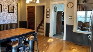 A dining area with a wooden table and metal chairs, a staircase, a clock, and a bookshelf with books.