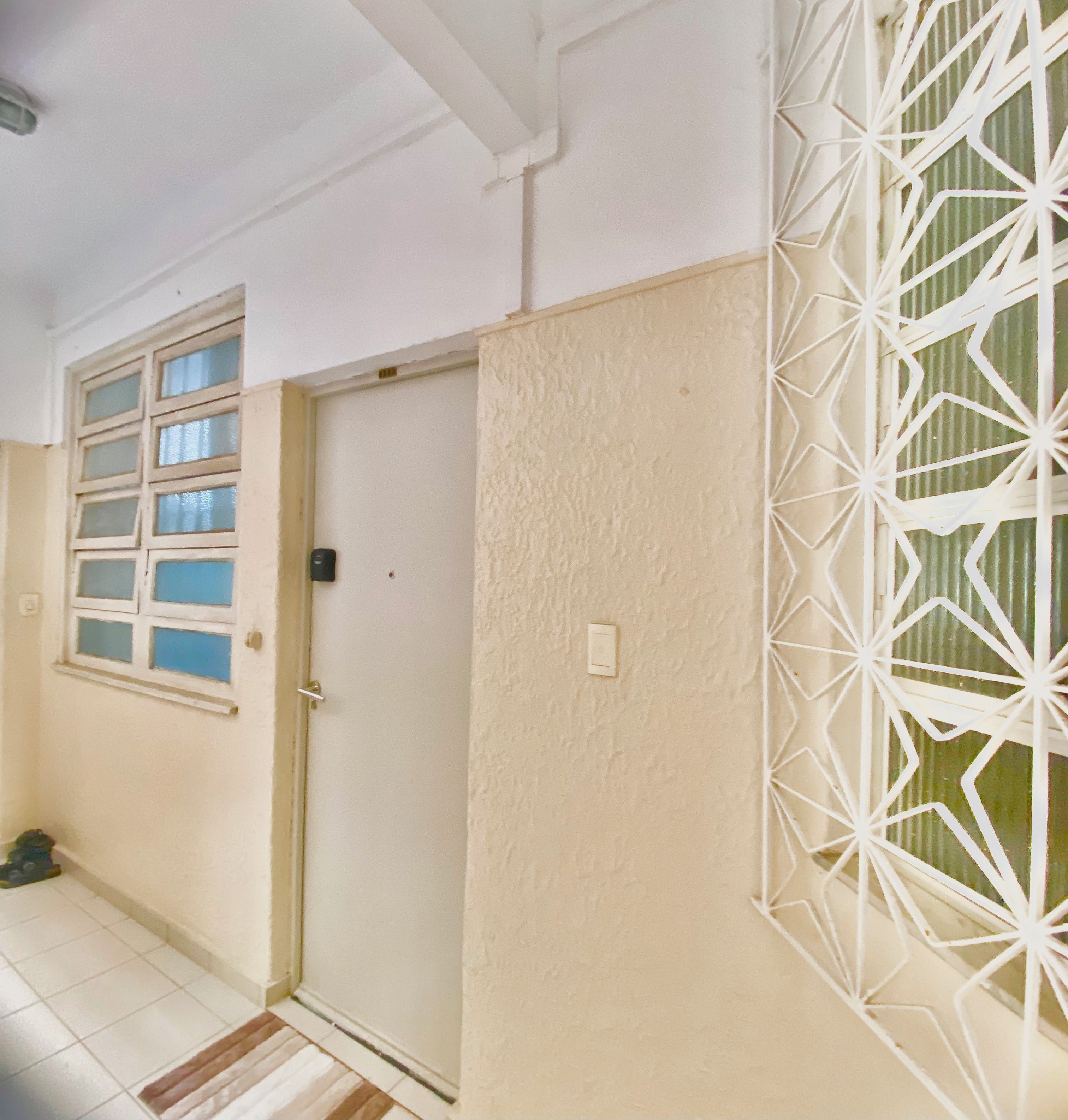 Un pasillo con una puerta, una ventana de varios cristales y una celosía metálica blanca decorativa en la pared.