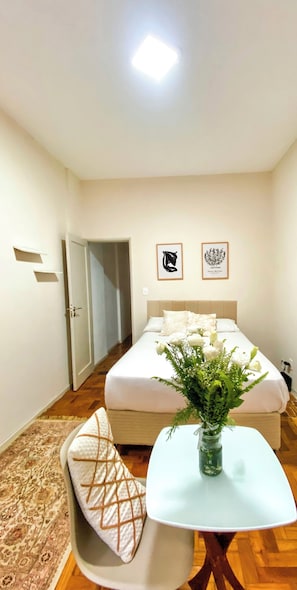 A hotel room with a bed, a bedside table with a vase of flowers, a chair, and two framed pictures on the wall.