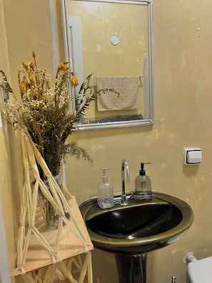 Een badkamer met een wastafel, spiegel, handdoekrek en een vaas met gedroogde bloemen.