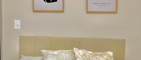 Un lit avec deux oreillers, une tête de lit et deux œuvres d’art encadrées accrochées au mur.