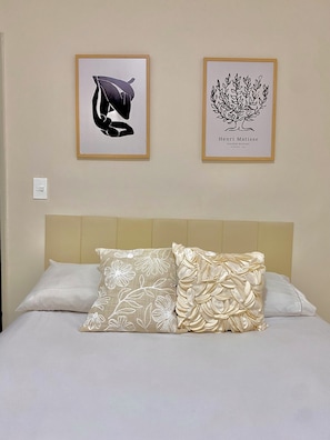 A bed with two pillows, a headboard, and two framed artworks on the wall.