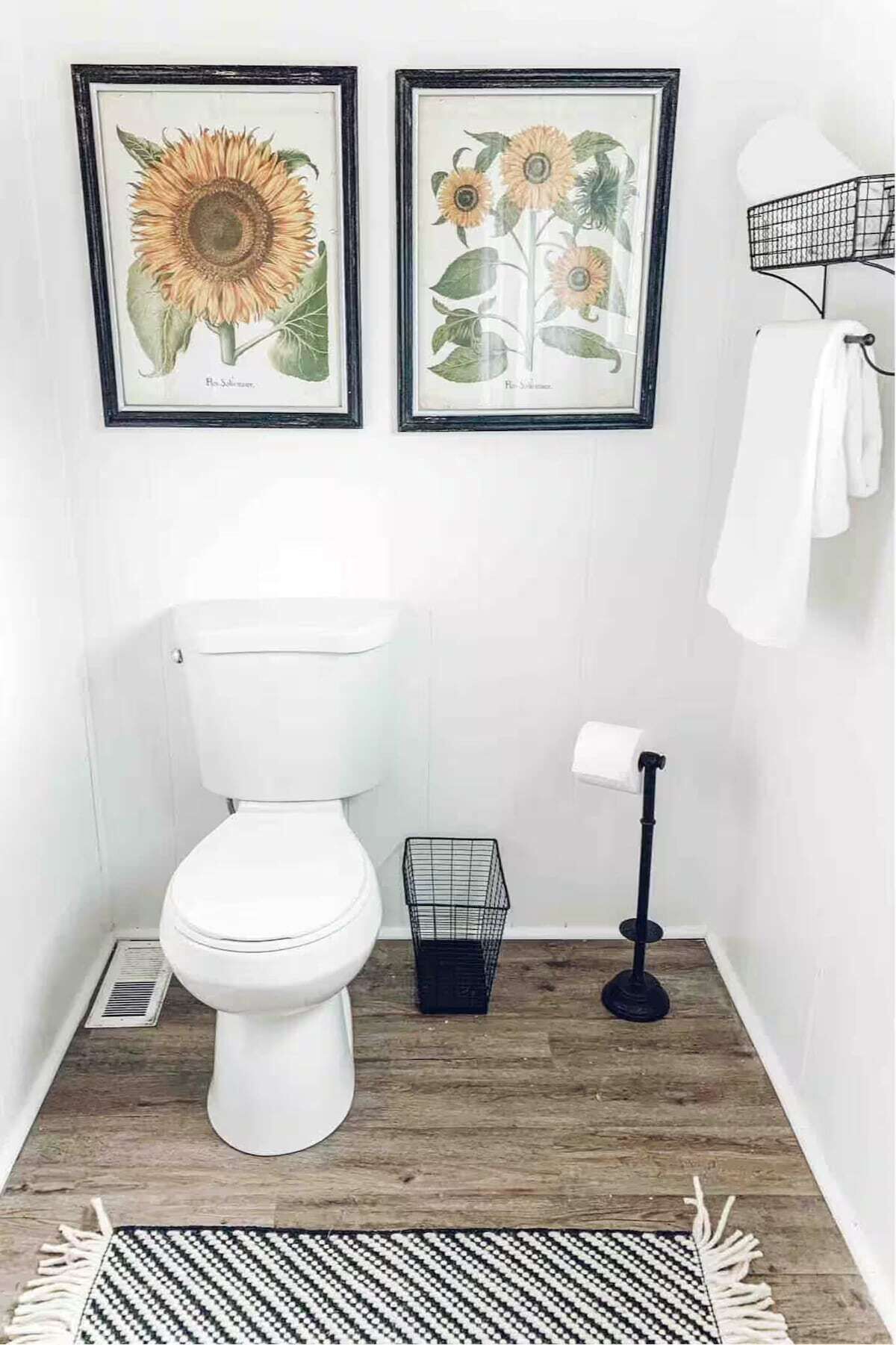 A bathroom with a white toilet, a black trash bin, and two framed botanical prints on the wall.