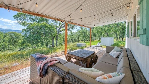 An outdoor patio with wicker furniture, a wooden table, and string lights. - Yosemite Boho Bungalow, Pet Friendly + Mtn Views! (Coarsegold)