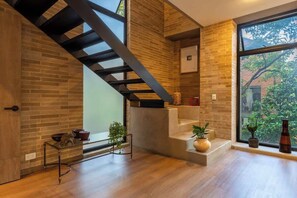 A modern interior with exposed brick walls, a concrete staircase, and large windows offering a view of greenery outside.