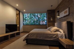 A modern bedroom with a large window, a bed, a TV, and a wooden bench.