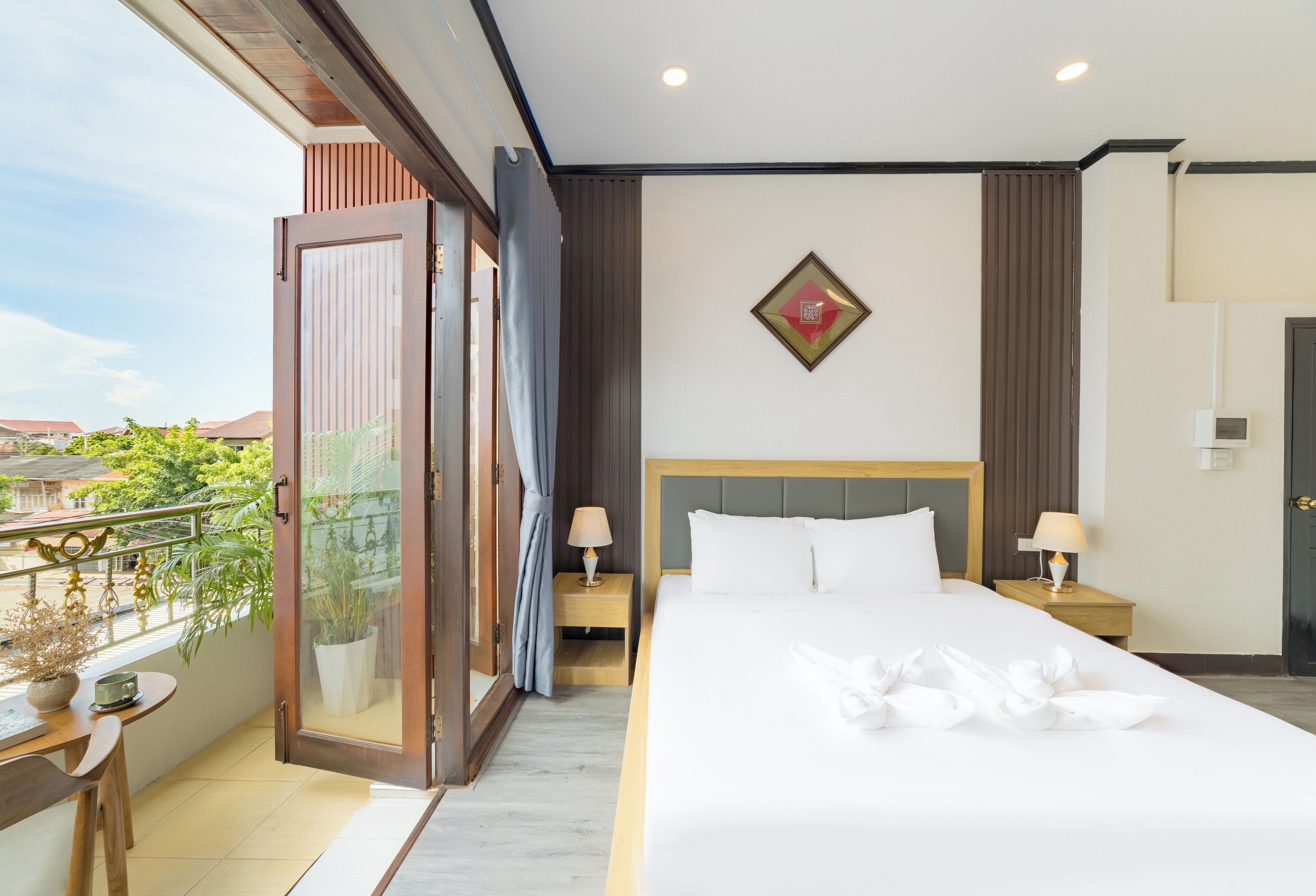 A hotel room with a large bed, two bedside tables with lamps, a view of the outdoors, and a decorative wall piece.