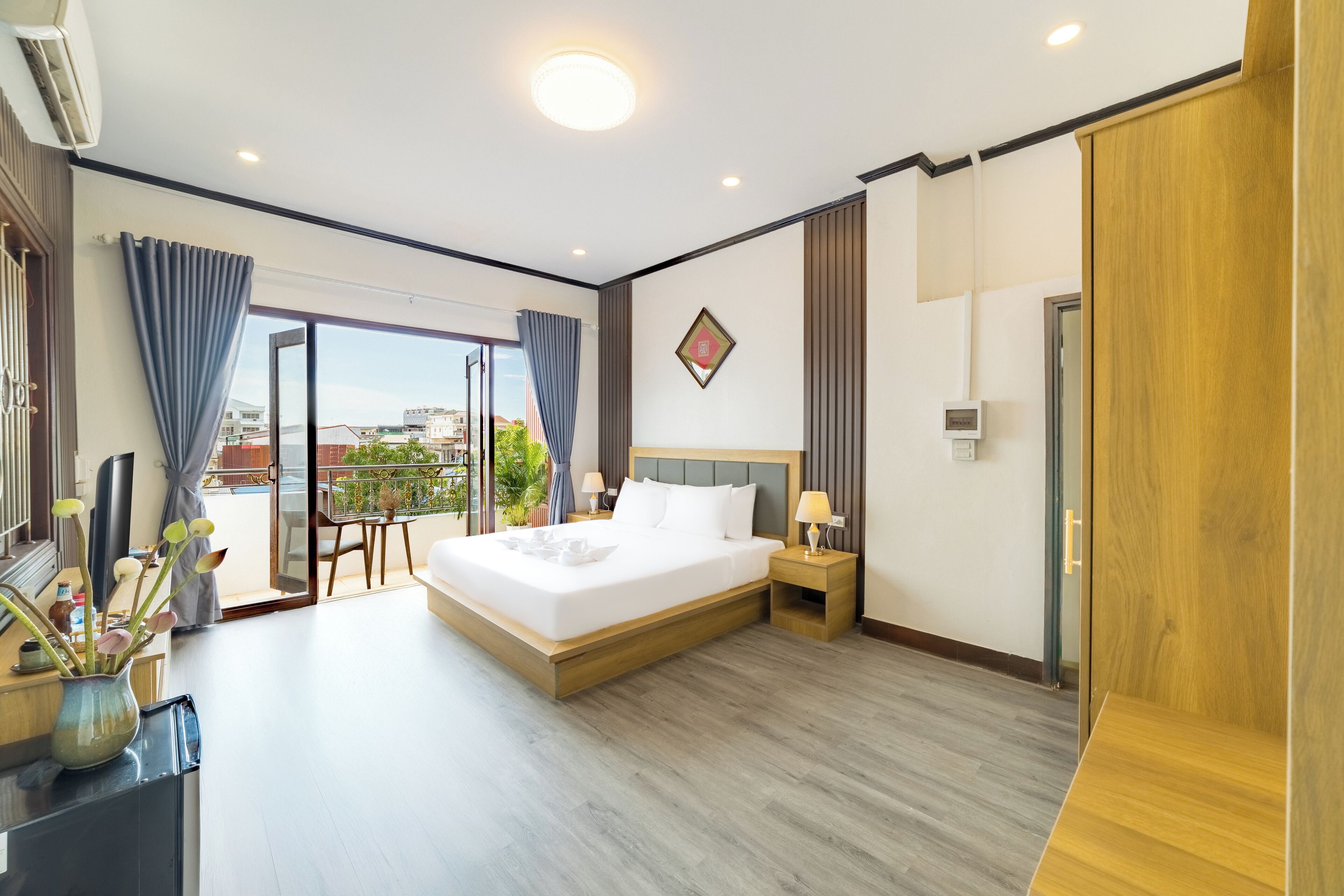 A modern hotel room with a large bed, a balcony with a view, and a wooden floor.