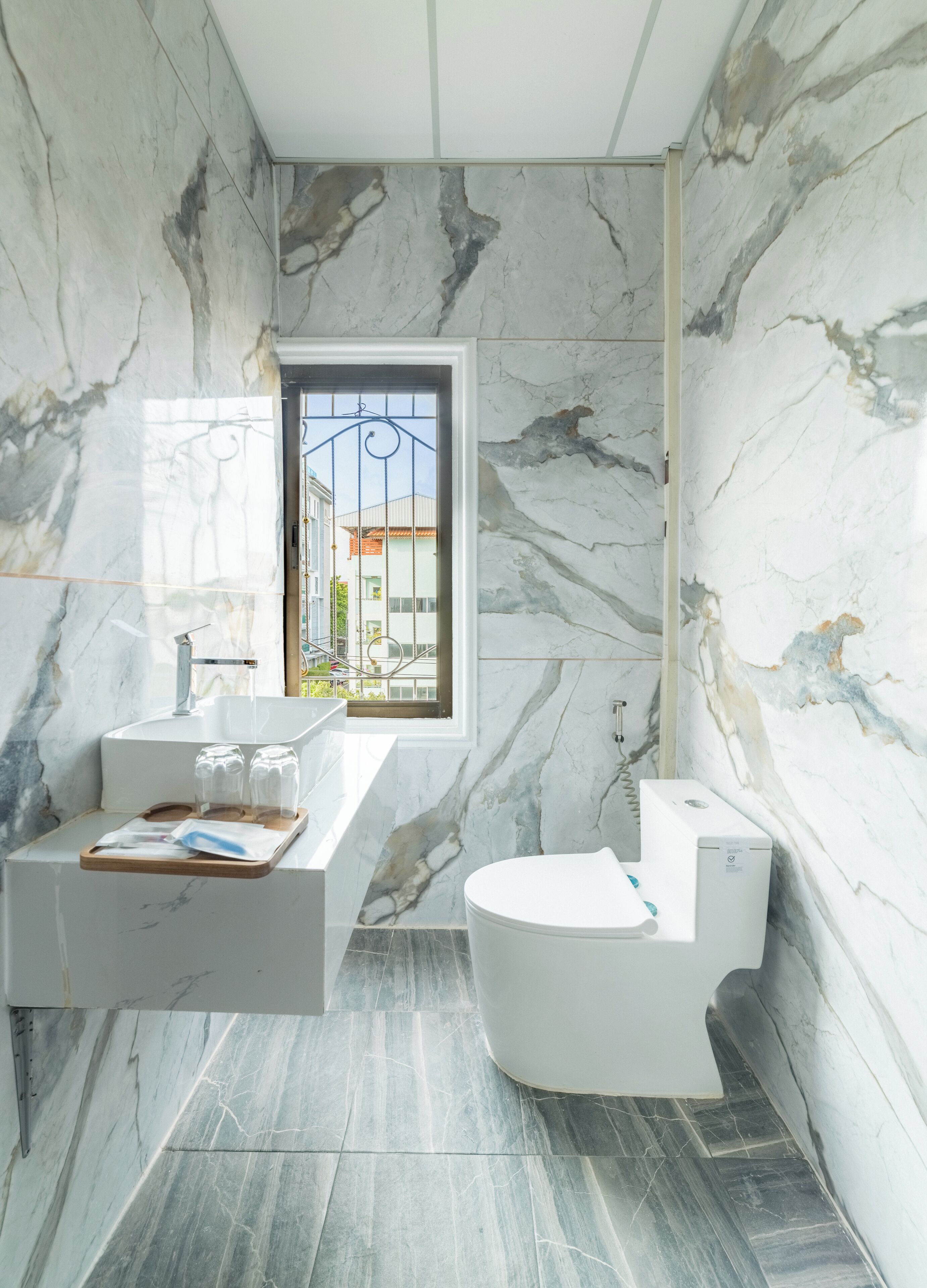 A bathroom with a marble wall, a white sink, a toilet, and a shower.
