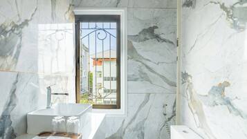 A bathroom with a marble wall, a white sink, a toilet, and a shower.