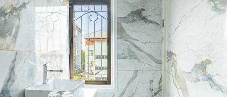 A bathroom with a marble wall, a white sink, a toilet, and a shower.
