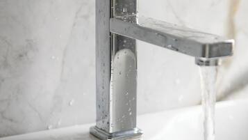 Ein modernes Badezimmer mit einem chromfarbenen Wasserhahn und klarem, fließendem Wasser.