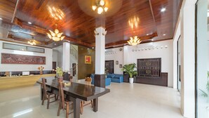 A spacious lobby with a wooden ceiling, a reception desk, a dining area with a table and chairs, and a blue sofa. - Peaceful 2 Hotel (Vientiane)
