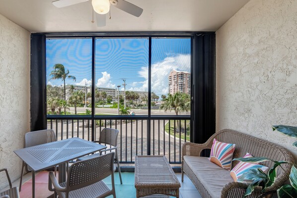 A balcony with wicker furniture, a table, and a sofa with colorful cushions. - ☀️Easy Beach Access | Great Amenities | Santa Maria 104- The Sunnyside☀️ (Fort Myers Beach)