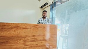 A wooden reception desk in a room with a large window and a view of the outside. - GLITZ PRIME MUMBAI INN (Mumbai)
