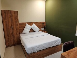 A single bed with a wooden headboard and white bedding, a wooden wardrobe, and a green wall. - GLITZ PRIME MUMBAI INN (Mumbai)