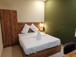 A single-bed room with a wooden headboard, white bedding, a bedside table with a lamp, and a green accent wall. - GLITZ PRIME MUMBAI INN (Mumbai)