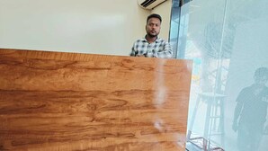 A wooden reception desk in a room with a large window and an air conditioning unit on the wall. - GLITZ PRIME MUMBAI INN (Mumbai)