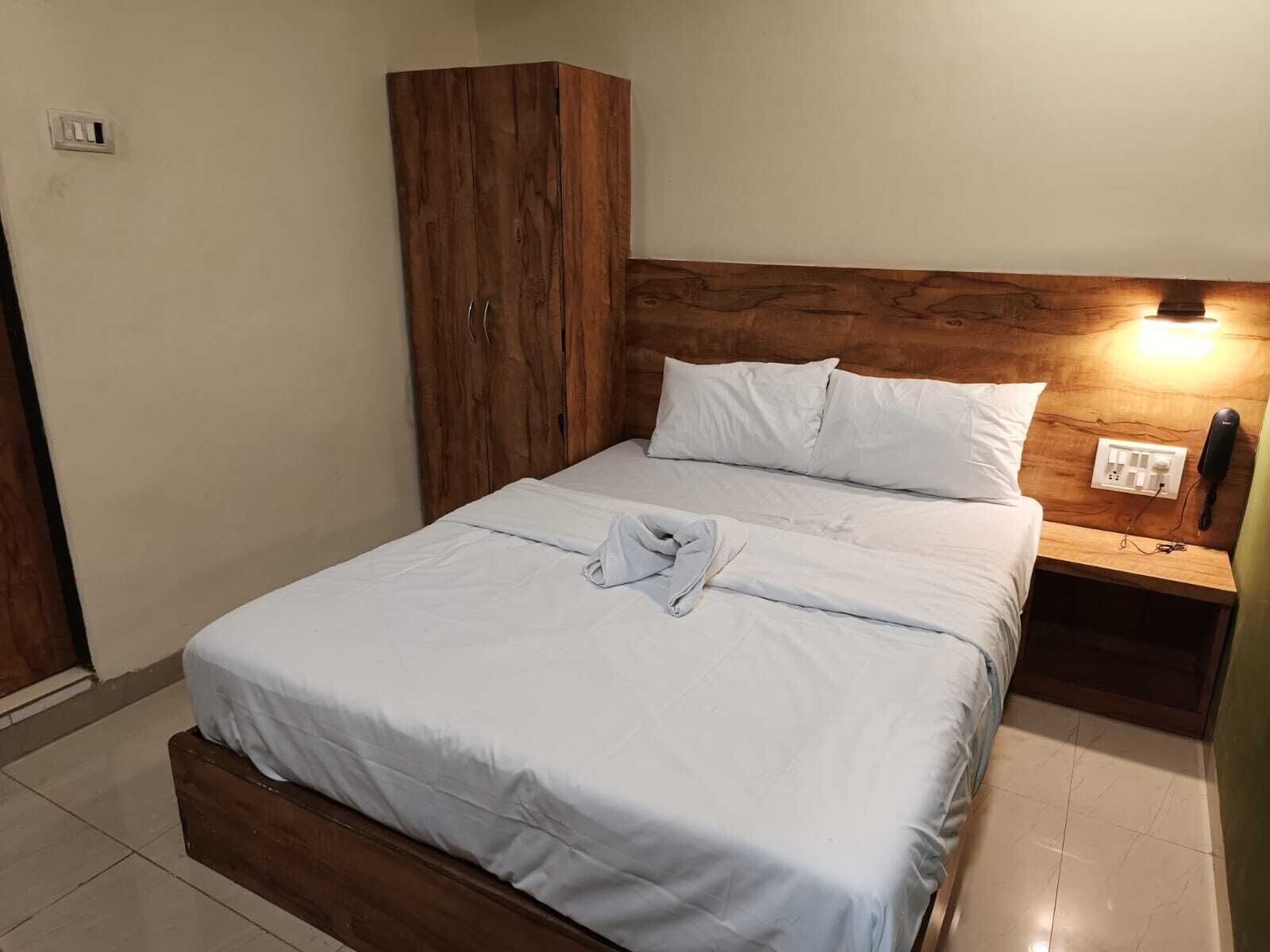 A neatly made bed with white linens, a wooden headboard, a bedside table with a lamp, and a wardrobe.