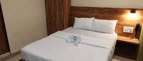 A neatly made bed with white linens, a wooden headboard, a bedside table with a lamp, and a wardrobe.
