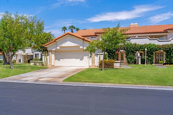 A residential house with a garage, a well-maintained lawn, and a clear blue sky. - Luxury Palm Desert Condo: Pool & Mountain Views (Palm Desert)