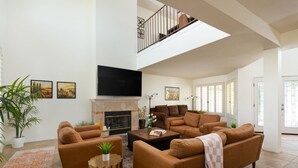 A spacious living room with a fireplace, a flat-screen TV, and a staircase leading to an upper level. - Luxury Palm Desert Condo: Pool & Mountain Views (Palm Desert)