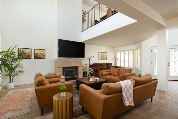 A spacious living room with a fireplace, a flat-screen TV, and a staircase leading to an upper level.
