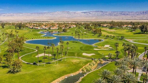 A golf course with multiple water hazards, palm trees, and a mountainous backdrop. - Luxury Palm Desert Condo: Pool & Mountain Views (Palm Desert)