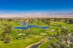 A golf course with multiple water hazards, palm trees, and a mountainous backdrop.