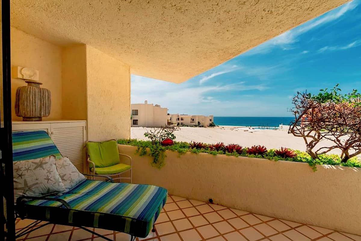 Ein Balkon mit einem gestreiften Stuhl, einem kleinen Tisch und Blick auf Strand und Gebäude in der Ferne.