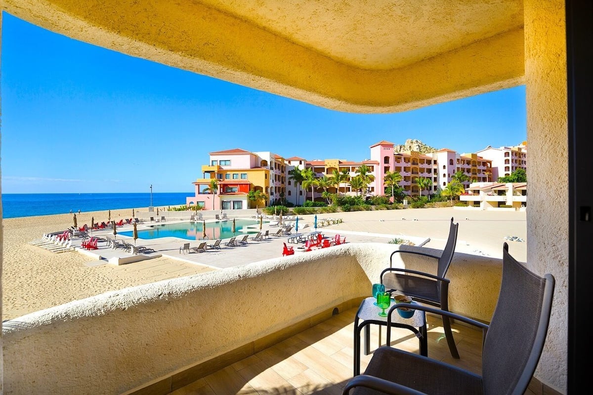 Ein Balkon eines Resorts mit Pool, Liegestühlen und Blick auf das Meer und die Hotelgebäude.