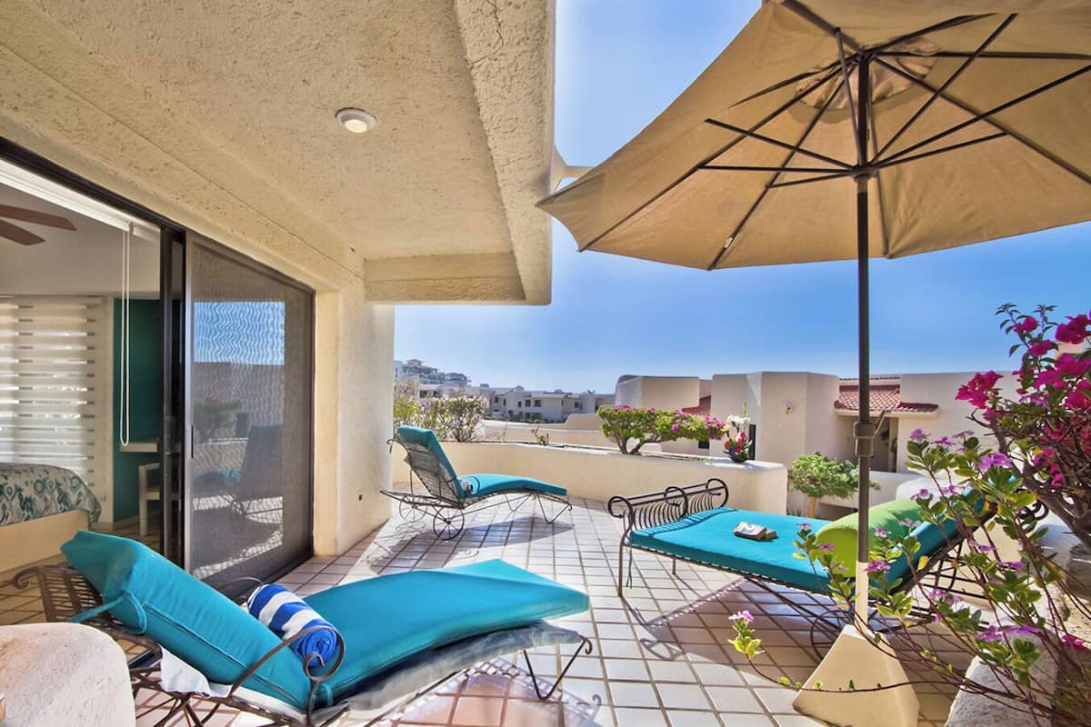 Ein Balkon mit zwei Liegestühlen, einem Tisch und einem Sonnenschirm.