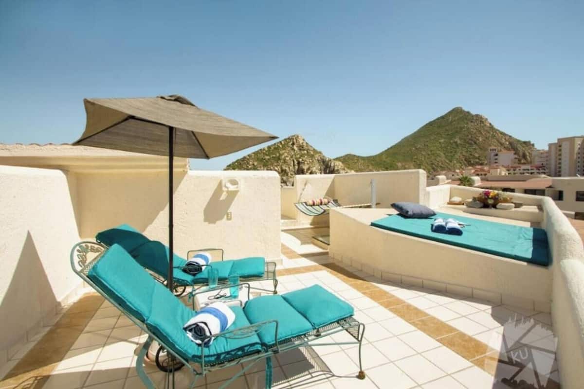 Eine Dachterrasse mit Liegestühlen, einem kleinen Tisch und einem großen Sonnenschirm.
